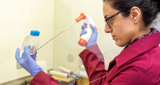 A female blood cancer researcher stands in a lab using a large pipette whilst looking at a sample in a small bottles.