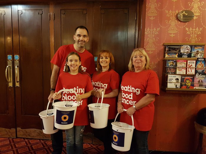 A group of fundraisers stand in a theatre with fundraising buckets. They're attending the musical "The Girls", written by Gary Barlow about the Calendar Girls.