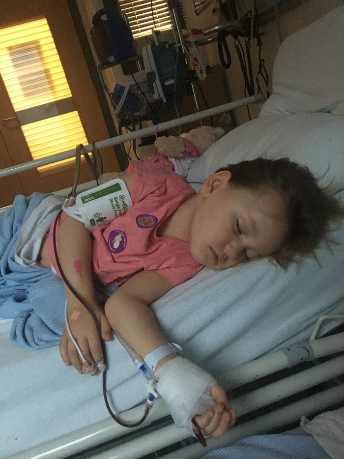 Mila Sneddon, who lives with acute lymphoblastic leukaemia (ALL), lies asleep in a hospital bed, with a blood catheter in her wrist.