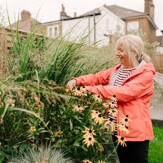 An older woman smiles as she works in her garden.