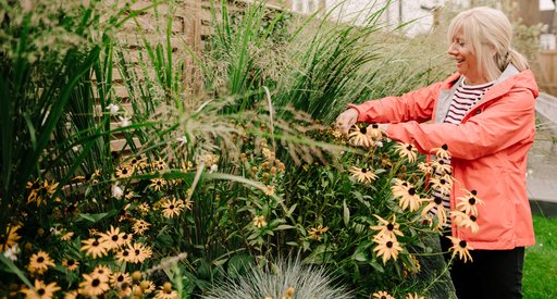 An older woman smiles as she works in her garden.