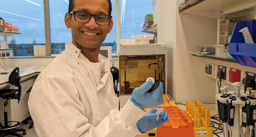 Dr Kiran Batta working in the lab smiling, wearing a white lab coat.