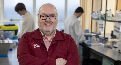 Professor Tonks stood in the lab, with his arms folded, wearing a red Blood Cancer UK lab coat.