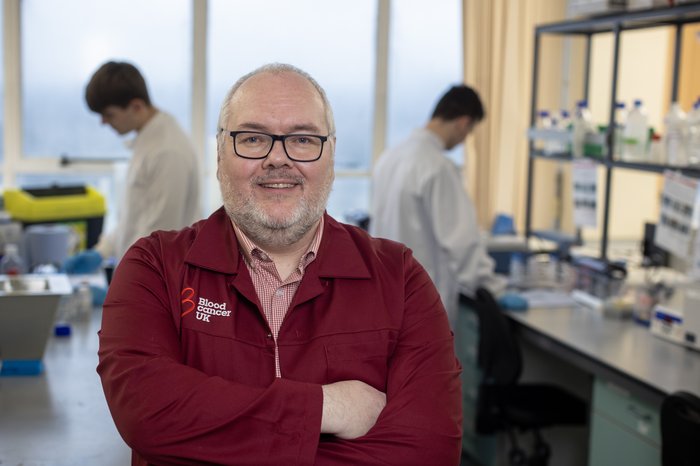 Professor Tonks stood in the lab, with his arms folded, wearing a red Blood Cancer UK lab coat.