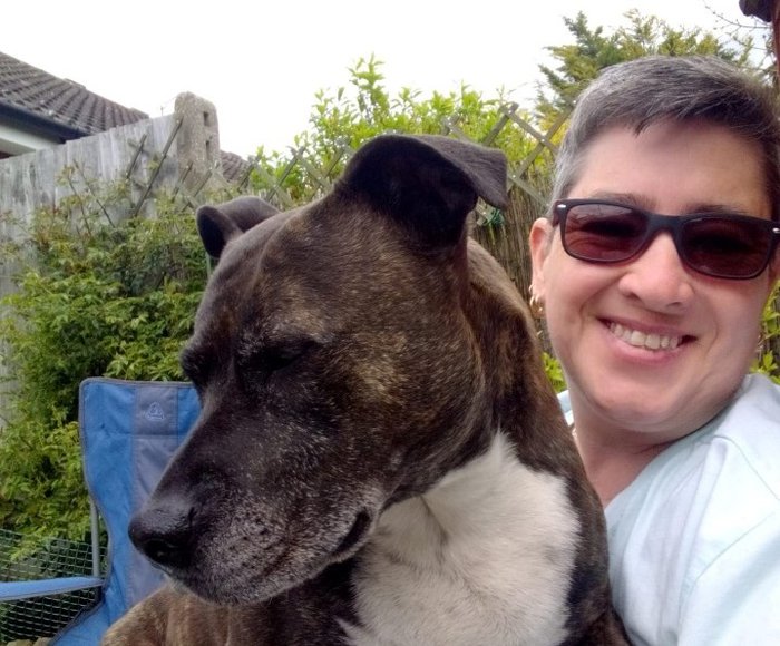 Angie Sharp who lives with CML, sits smiling in the garden with a large dog on her lap.