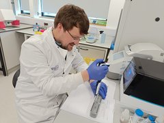 A man sat in a science lab wearing a white lab coat performing an experiment.