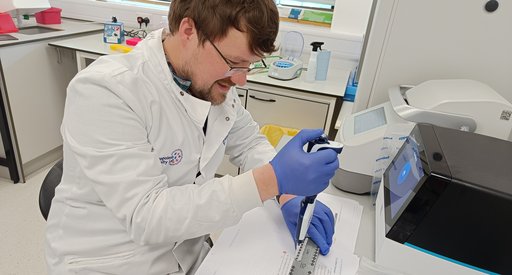 A man sat in a science lab wearing a white lab coat performing an experiment.