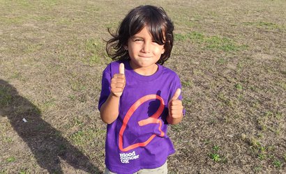 A young boy wearing a Blood Cancer UK shirt smiles at the camera with his thumbs up.