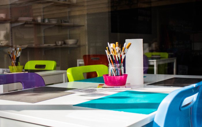 A stock image of a school desk with blue writing mats and purple and green chairs tucked into the table.