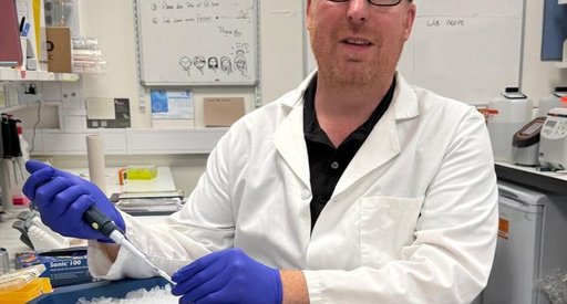 A man sat holding a pipette working in the lab, wearing a white lab coat.