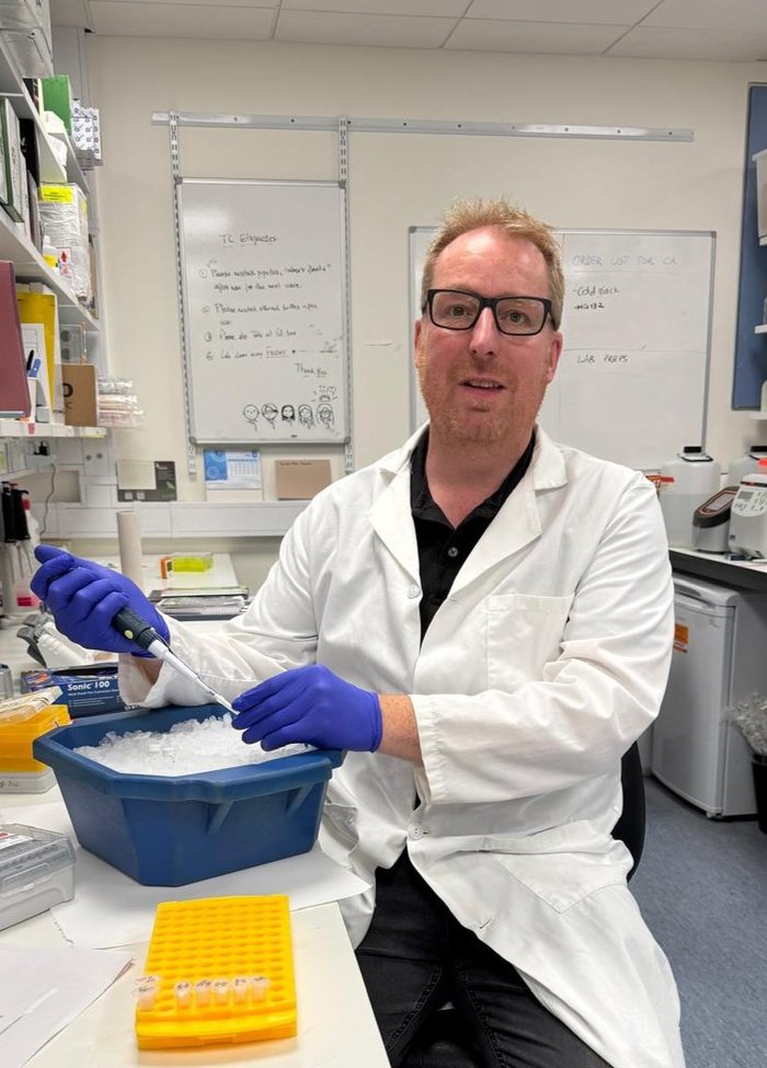 A man sat holding a pipette working in the lab, wearing a white lab coat.