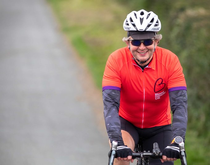 A cyclist heading down a country lane wearing a red Blood Cancer UK T shirt.