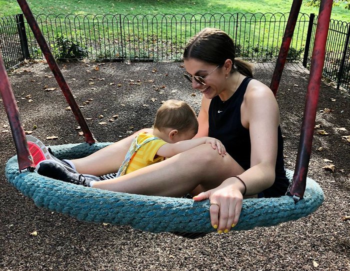 A mother and child playing on a swing in the playground on a sunny day, laughing and having fun.