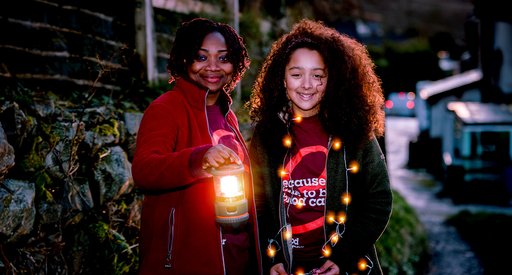 Two people smiling and holding lanterns under a moon-lit sky at a Walk of Light event.