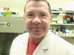 A headshot of a man with spikey hair wearing a white lab coat in the lab.