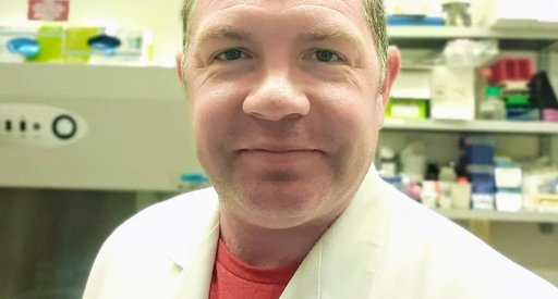 A headshot of a man with spikey hair wearing a white lab coat in the lab.