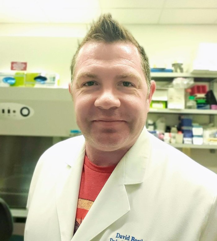 A headshot of a man with spikey hair wearing a white lab coat in the lab.