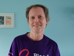 David, who has a type of blood cancer called chronic lymphocytic leukaemia (CLL). He's wearing a Blood Cancer UK T-shirt and is standing in front of a blue wall.