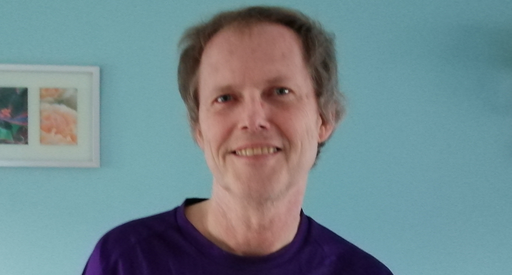 David, who has a type of blood cancer called chronic lymphocytic leukaemia (CLL). He's wearing a Blood Cancer UK T-shirt and is standing in front of a blue wall.