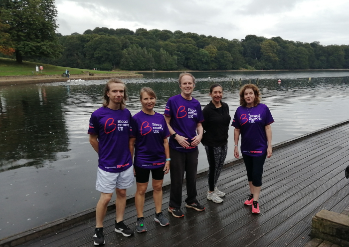 A group of five people pose together on decking next to a river; they wear purple Blood Cancer UK T shirts.