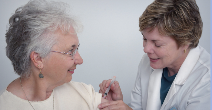 A female doctor in a lab coat injecting a female blood cancer patient at the top of her arm.