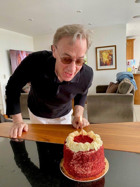 Doug leaning down to blow out a single candle on a cake.