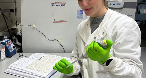 An image of a lady wearing a white lab coat using a pipette in a science lab.