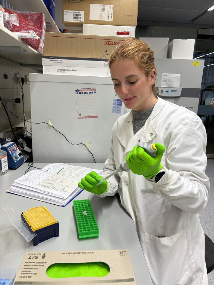 An image of a lady wearing a white lab coat using a pipette in a science lab.