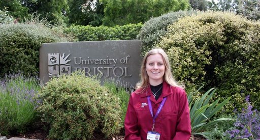 A lady stood outside by a University of Bristol sign wearing a red Blood Cancer UK lab coat.