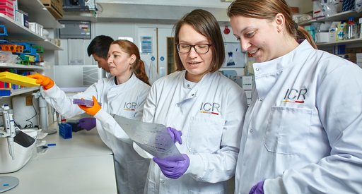 A lady working in the lab with other members of the lab team, all wearing white lab coats.