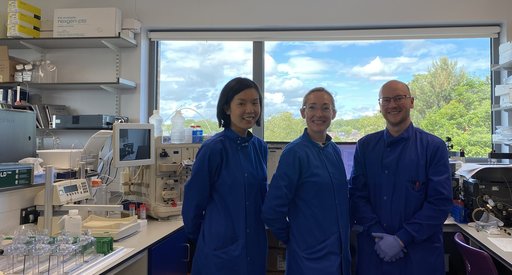 Dr Sean Lim and two other lab team members stood together in the lab wearing blue lab coats.