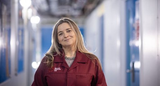 A lady stood wearing a red Blood Cancer UK lab coat, smiling at the camera.