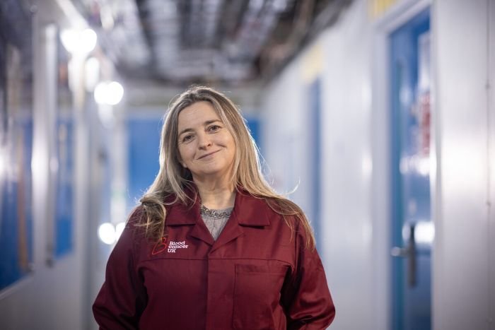 A lady stood wearing a red Blood Cancer UK lab coat, smiling at the camera.