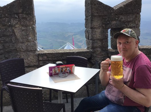 Franko, blood cancer patient, drinking a large beer from a glass. Mountainous view in the background.