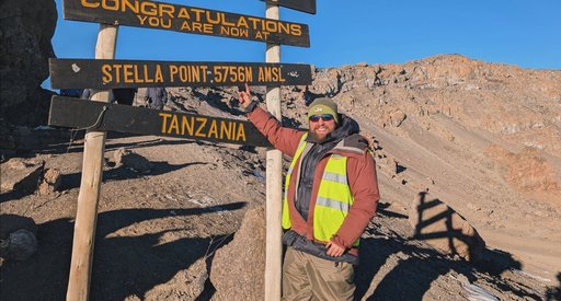 George stands in front of a sign on Mount Kilimanjaro