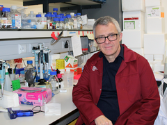Professor George Vassiliou sat in the lab smiling wearing his lab coat.