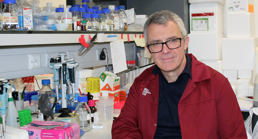 Professor George Vassiliou sat in the lab smiling wearing his lab coat.