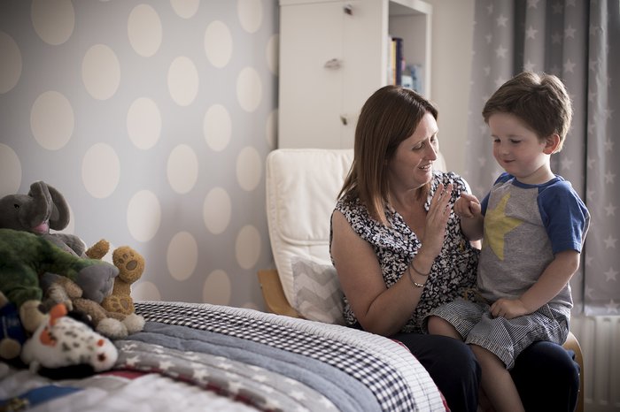 Hugo, in remission from leukaemia, propped on her knee and looking towards a grouping of cuddly toys.