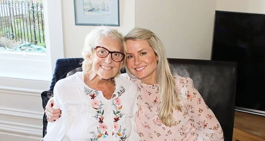 Two women sitting on a sofa with their arms around one another, smiling.