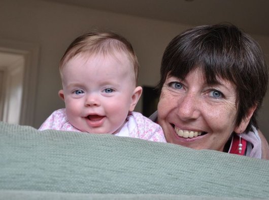 Image of a lady with short brown hair smiling at the camera alongside a baby