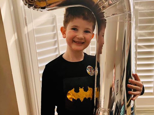 Hugo, who was diagnosed with blood cancer, holding a number seven balloon on his birthday in a living room.