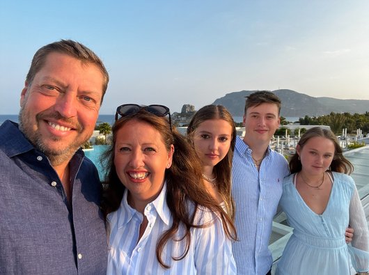 Matthew Wilson stands smiling with his family on a sunny evening in Summer.