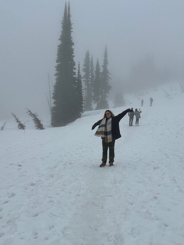 Jess on a snowy hillside. She's smiling with her arms raised.