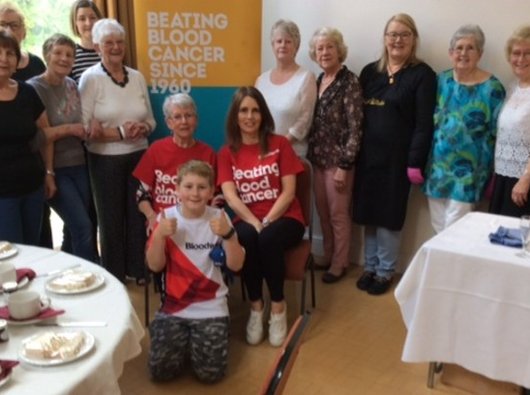 Johanna, who is affected by blood cancer, sat with friends in front of a Bloodwise banner.