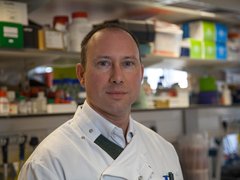 Headshot of Dr John Riches in the lab wearing his lab coat.