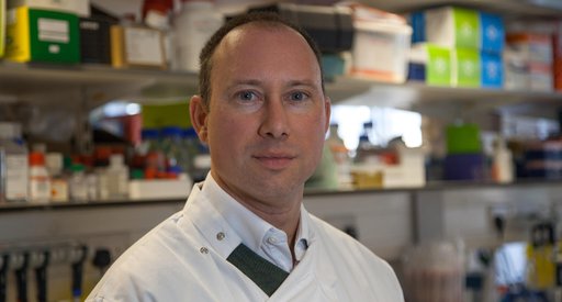 Headshot of Dr John Riches in the lab wearing his lab coat.