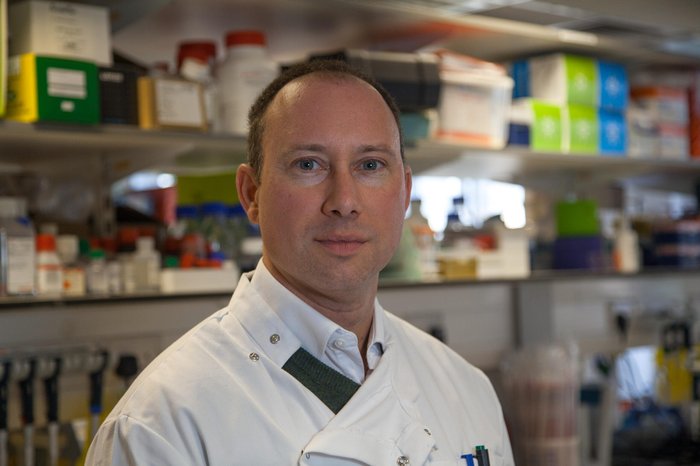Headshot of Dr John Riches in the lab wearing his lab coat.