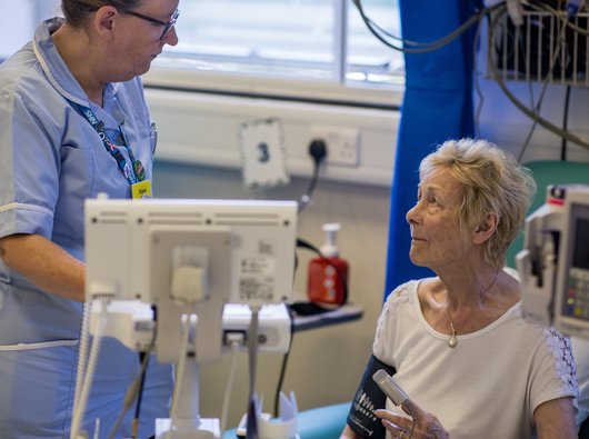 A female patient sits down while she has her blood pressure and heart rate checked by a nurse.