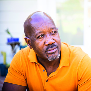 An older middle-aged Black man in an orange shirt.
