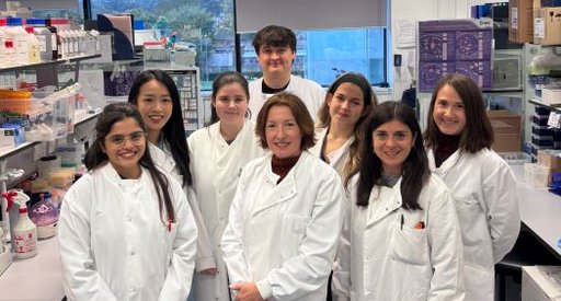 A group of eight people stood in the lab, wearing white lab coats, smiling at the camera.